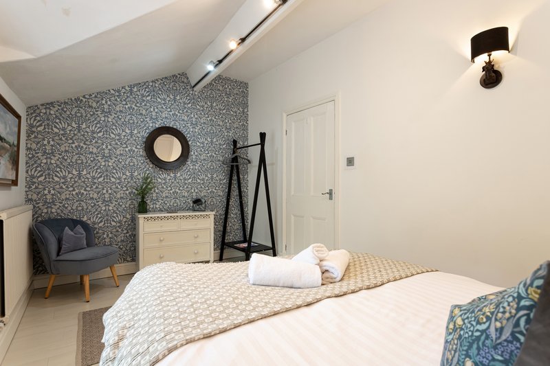 Modern bedroom with double bed, patterned accent wall, chair and storage furniture