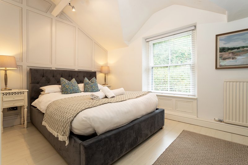 Bright bedroom with gray upholstered bed, cream bedding, twin bedside lamps, and large window