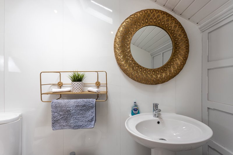 Modern bathroom with round gold mirror, wall-mounted brass shelf, white sink and toilet