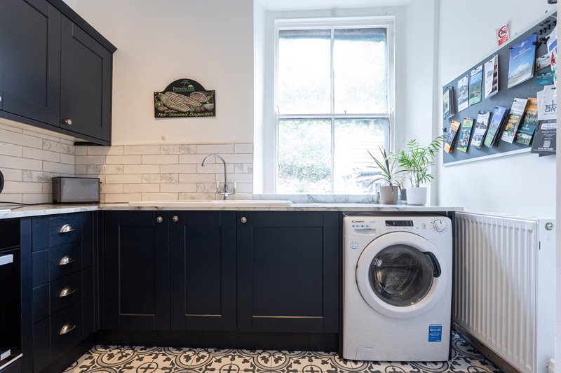 Modern kitchen with dark cabinetry, subway tile backsplash, window, washing machine and radiator