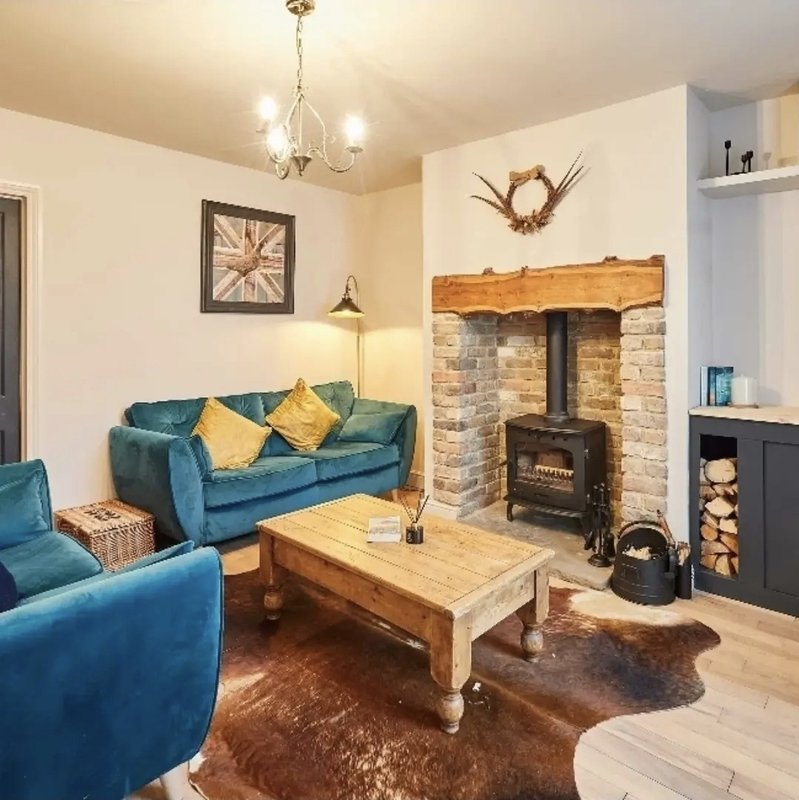Living room with teal sofa, wood coffee table, wood-burning stove and brick fireplace