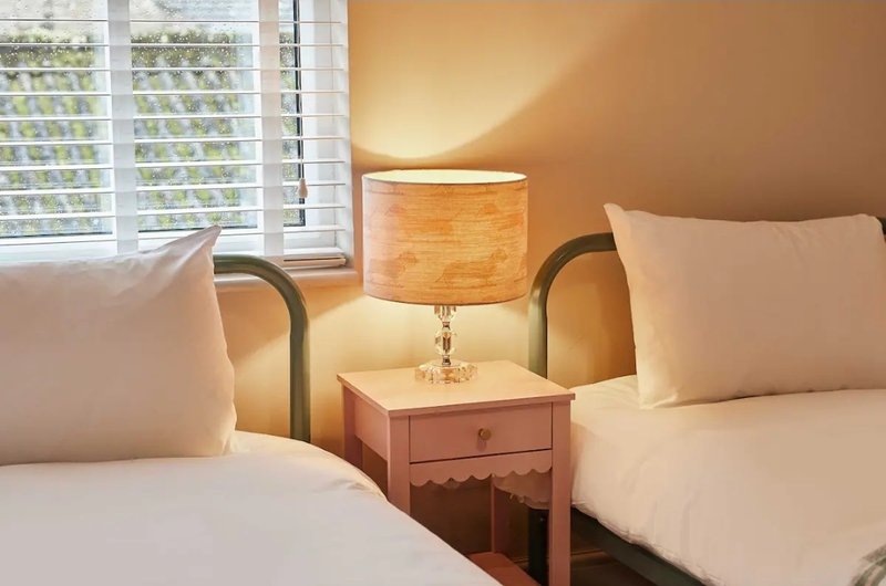 Bright bedroom with two single beds, wooden bedside table, lamp and window with shutters