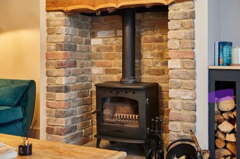 Living room with black wood-burning stove set in red brick fireplace, teal armchair visible left