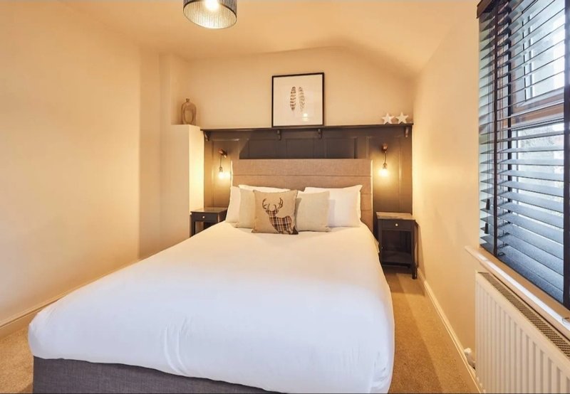Modern bedroom with double bed, dark headboard, bedside lamps, and window with shutters