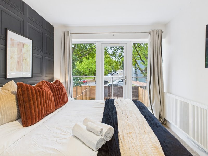 Bright bedroom with double bed, orange cushions, balcony doors and garden views