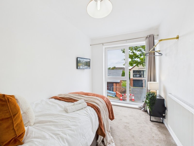 Bright bedroom with single bed, white bedding, orange throw, and glass door leading to balcony