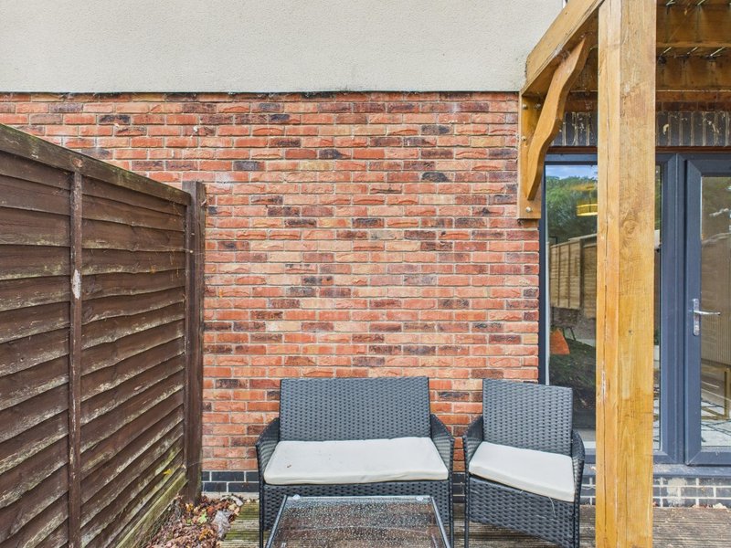 Brick patio with two cushioned chairs and wooden pergola frame