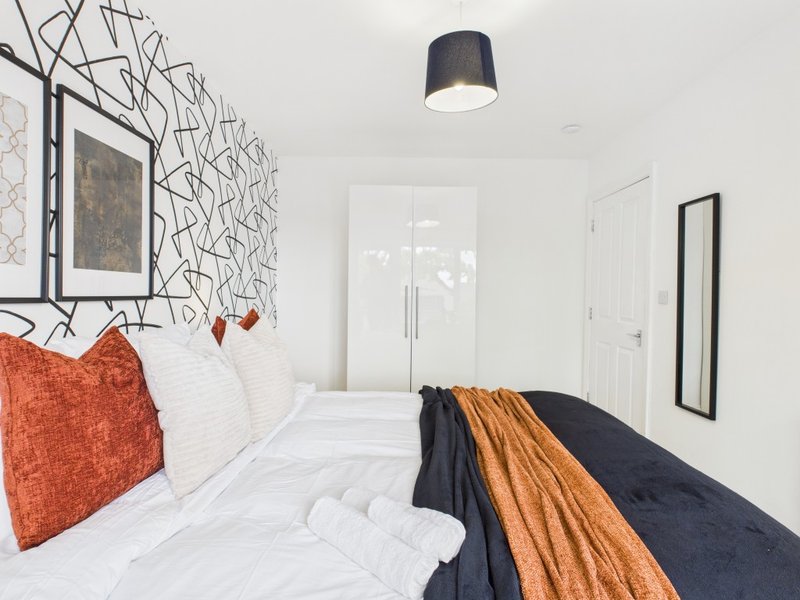 Modern bedroom with double bed, orange cushion, white bedding, patterned wallpaper and pendant light