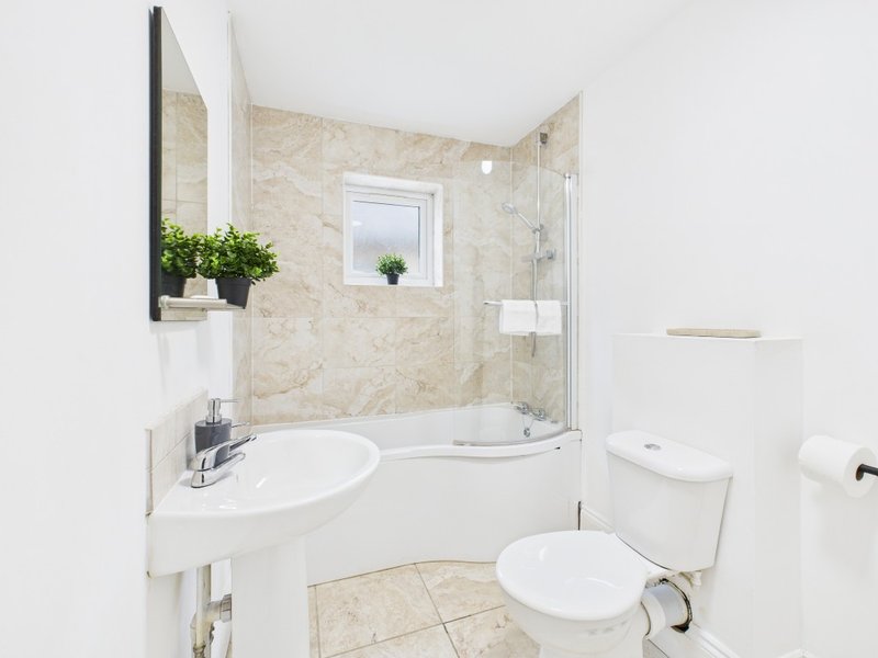 Modern bathroom with white sink, toilet, shower enclosure and beige tile walls
