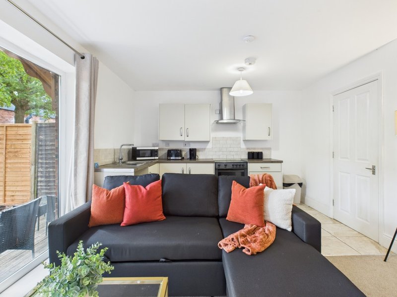 Open-plan living area with black sofa, orange cushions, and integrated kitchen with white cabinets