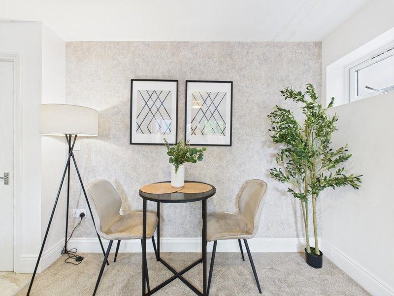 Modern sitting area with round table, two beige chairs, floor lamp, and potted plants
