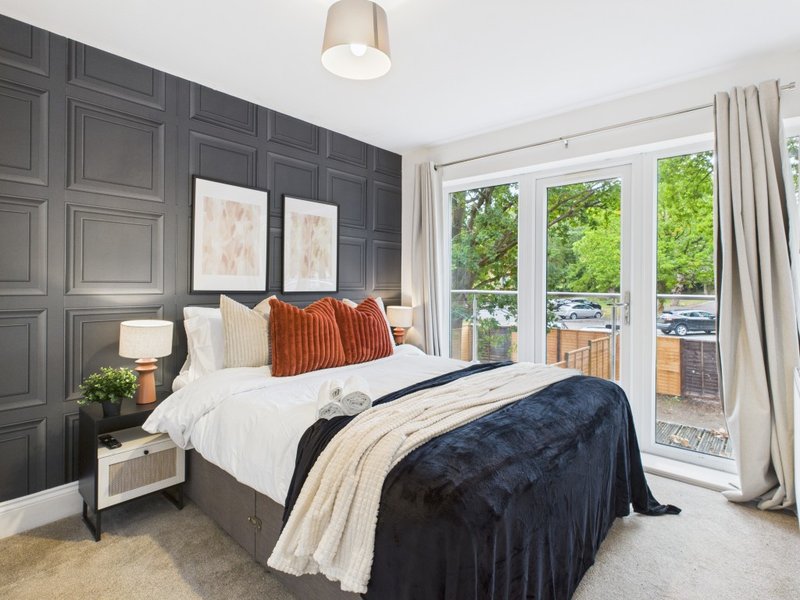 Modern bedroom with dark feature wall, double bed, orange cushions, and glass doors to balcony