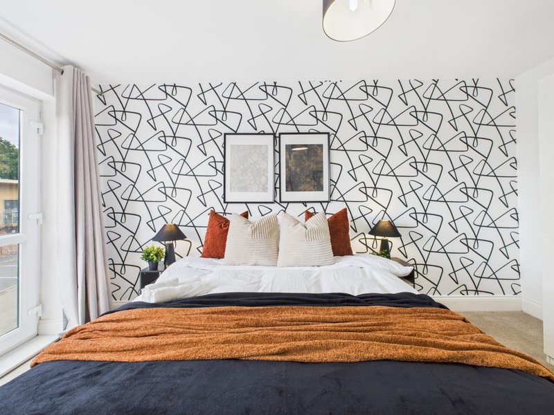 Modern bedroom with patterned accent wall, double bed with orange throw, white pillows, and framed artwork