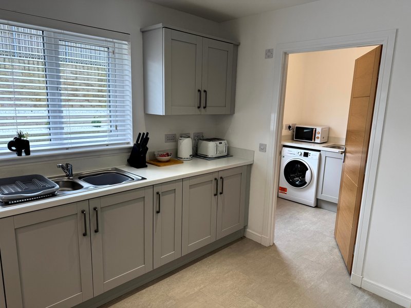 Modern kitchen with grey cabinetry, induction hob, and view into utility room with washing machine