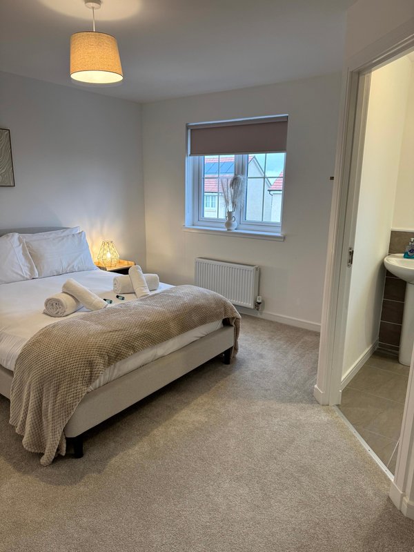 Bright bedroom with double bed, pendant light, bedside lamp and en-suite doorway