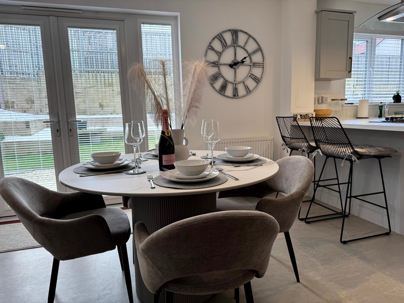 Modern dining area with round white table, grey upholstered chairs, place settings and wine bottle