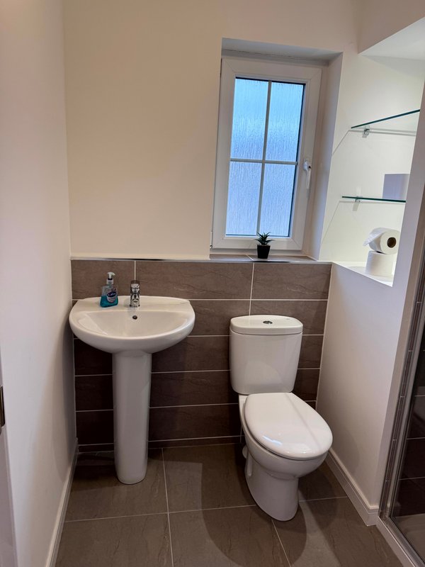 Small bathroom with pedestal sink, toilet, window, and tiled walls