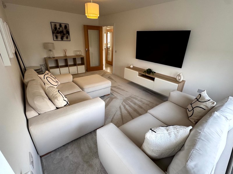 Modern living room with large cream sectional sofa, wall-mounted TV, and pendant light fixture