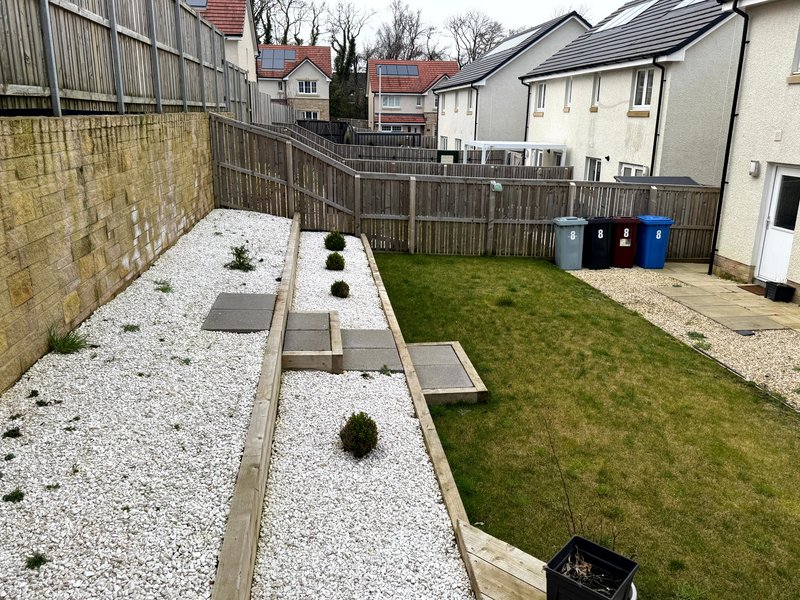 Rear garden with lawn, gravel border, wooden fence, and residential properties visible