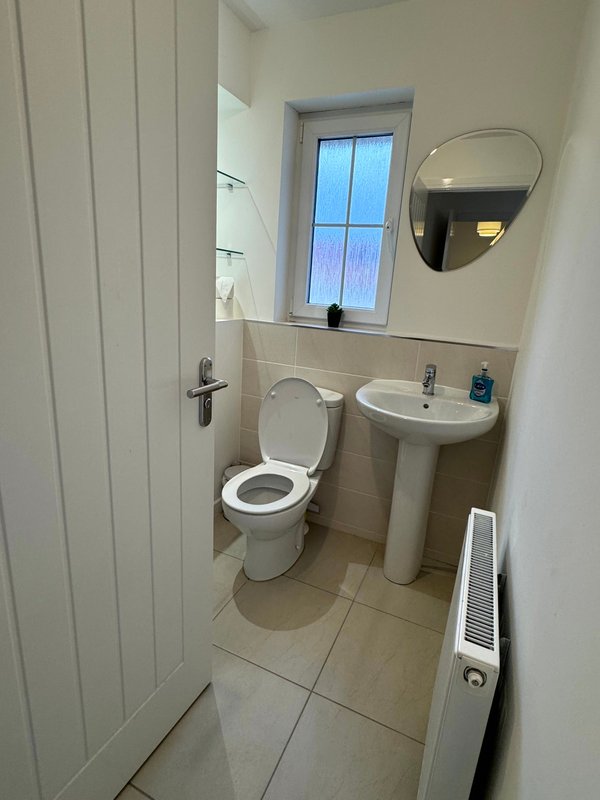 Small bathroom with toilet, pedestal sink, mirror and window