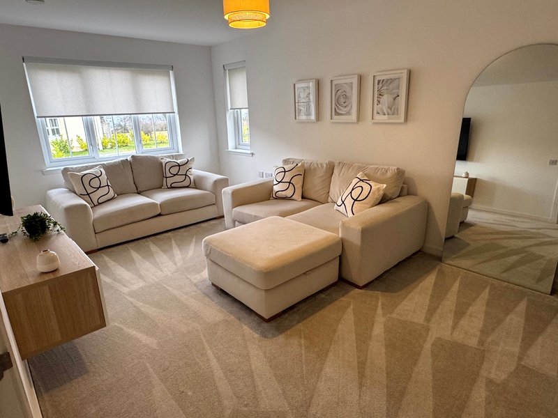 Spacious living room with beige sofas, cream ottoman, wooden side table, and large mirror