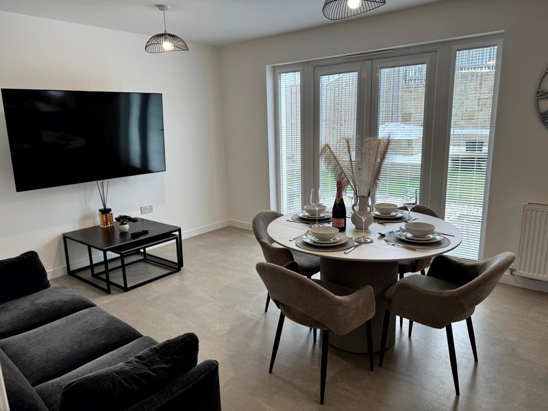 Modern open-plan living and dining area with wall-mounted TV, round dining table, chairs and sofa