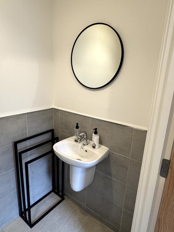 Modern bathroom with pedestal sink, round mirror, grey tile walls, towel rack