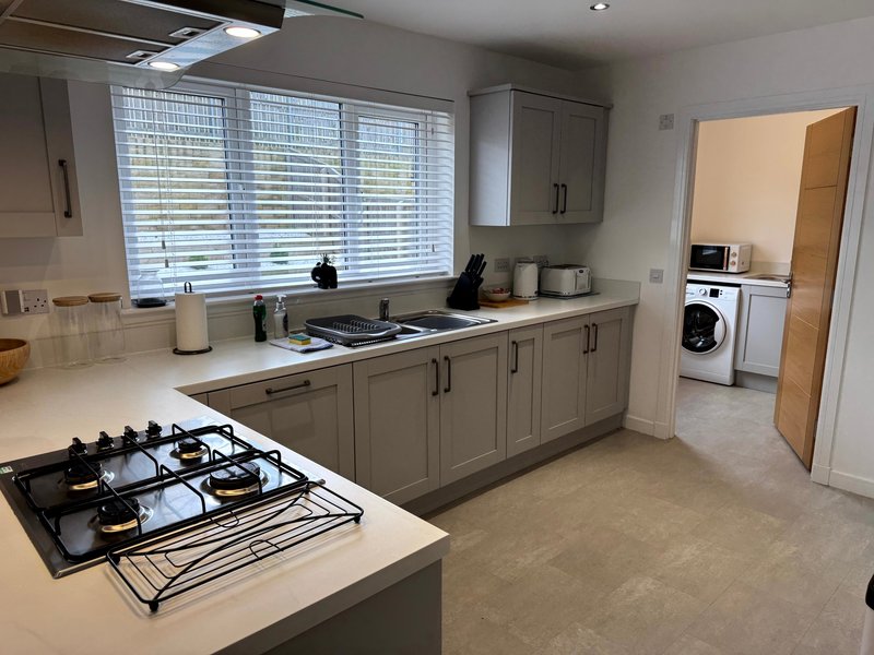 Modern kitchen with gas hob, grey cabinetry, window blinds and adjoining utility area