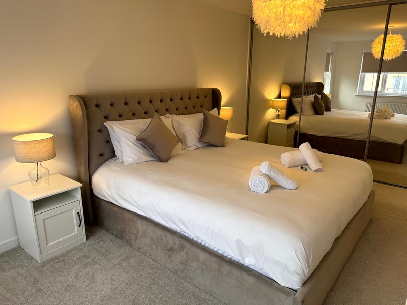 Modern bedroom with upholstered bed, white pillows, rolled towels, bedside lamp and mirror wardrobe