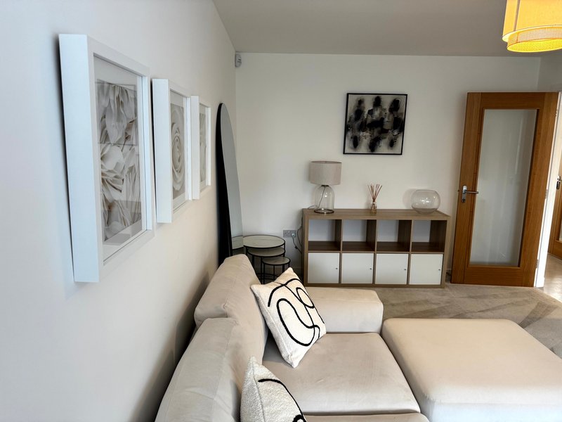 Modern living room with beige sectional sofa, storage shelving unit, framed wall art and wooden door