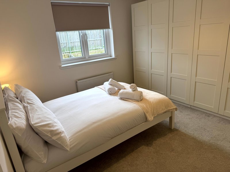 Bright bedroom with double bed, white bedding, cream wardrobe and window with roller blind