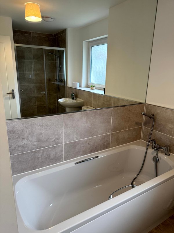 Modern bathroom with white bathtub, grey tile surround, glass shower enclosure and window