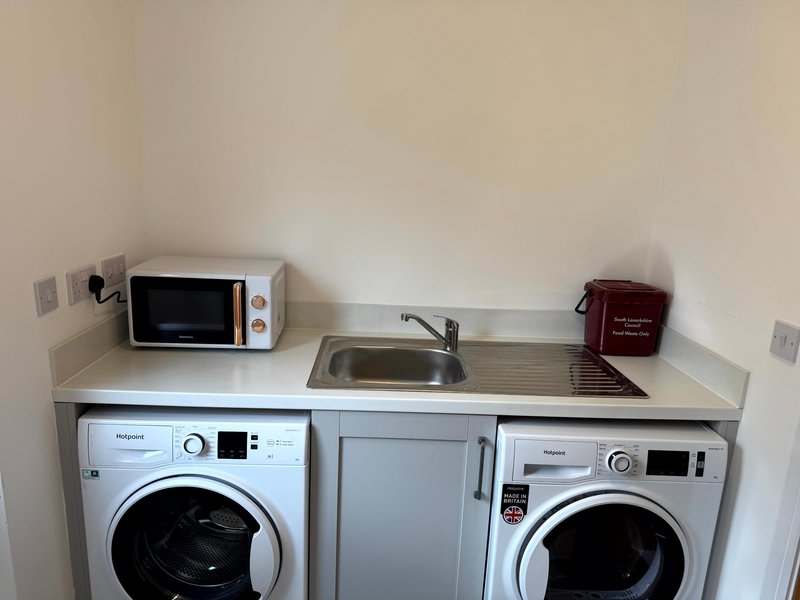 Laundry room with two washing machines, sink, microwave and storage cabinet