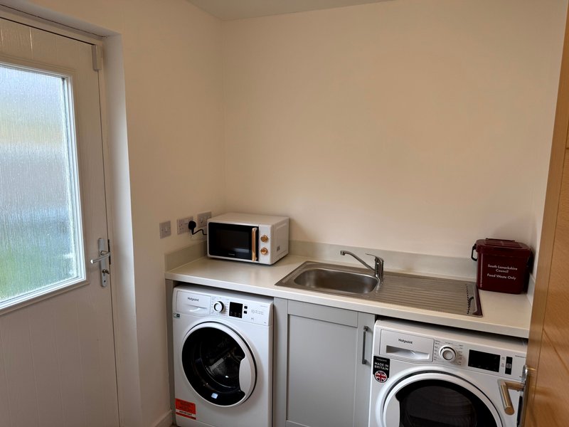 Utility room with washing machine, dryer, sink, microwave and door to garden