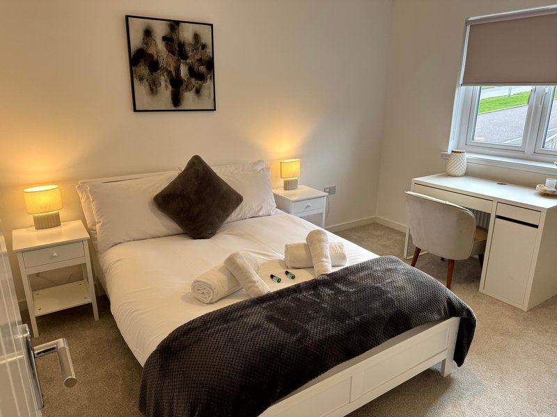 Bright bedroom with double bed, white bedding, dark throw, bedside tables and desk by window