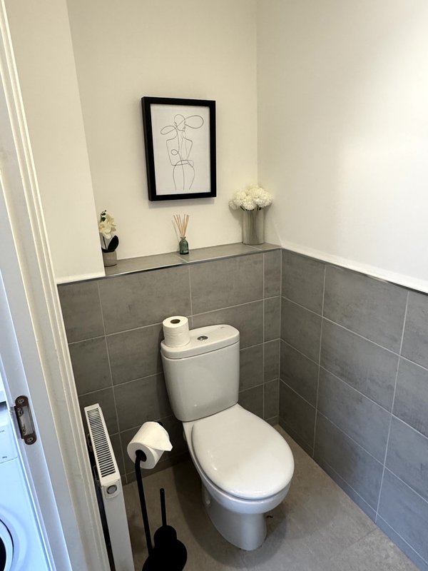 Modern toilet room with grey tile walls, white toilet, framed line art, and bathroom accessories