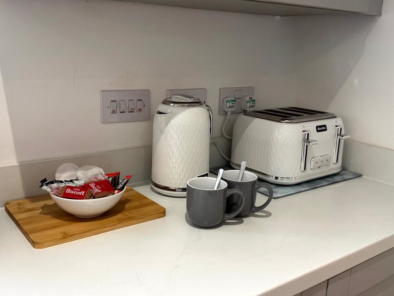 Kitchen counter with kettle, toaster, mugs, and bowl of items on wooden board