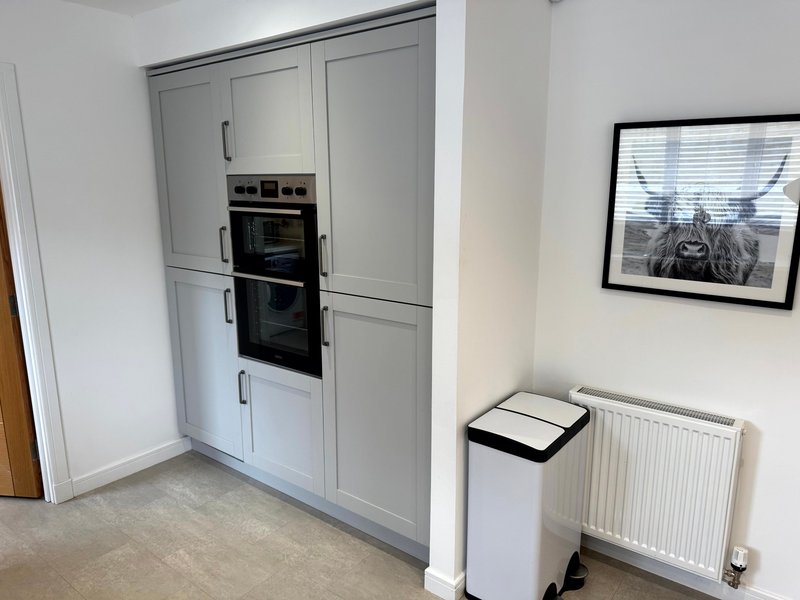 Modern kitchen with white cabinetry, built-in ovens, radiator and framed artwork