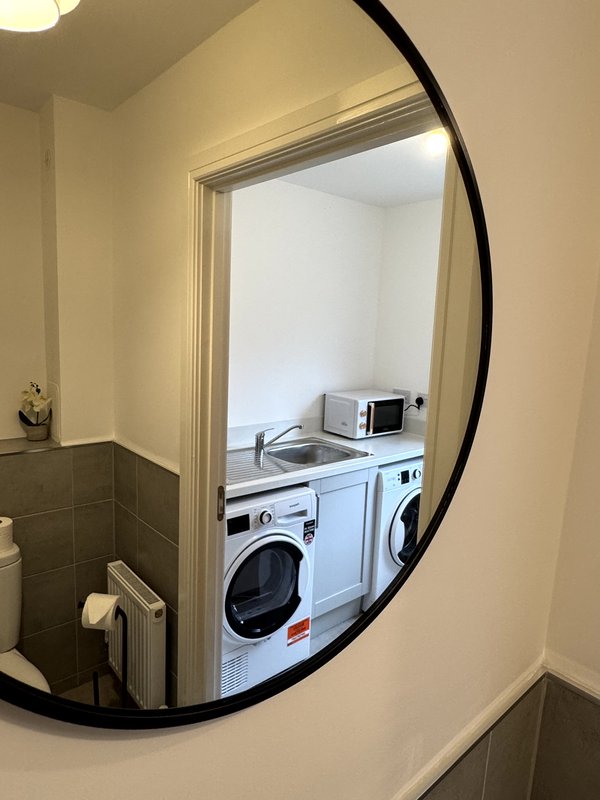 Laundry room with washing machine, tumble dryer, and sink reflected in round mirror
