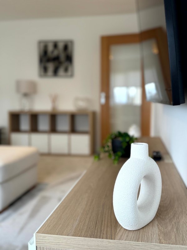 Modern bedroom with wooden furniture, white decorative vase on dresser, and storage unit