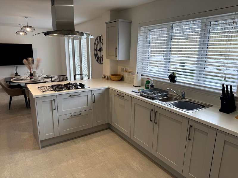 Modern kitchen with white cabinetry, gas hob, island unit, and dining area visible in background
