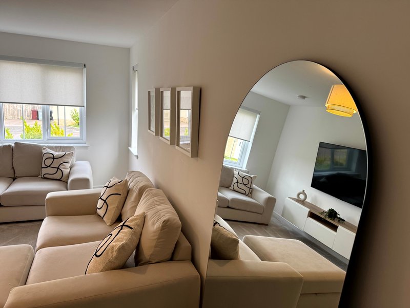 Modern living room with beige sectional sofa, round mirror, and natural light from windows