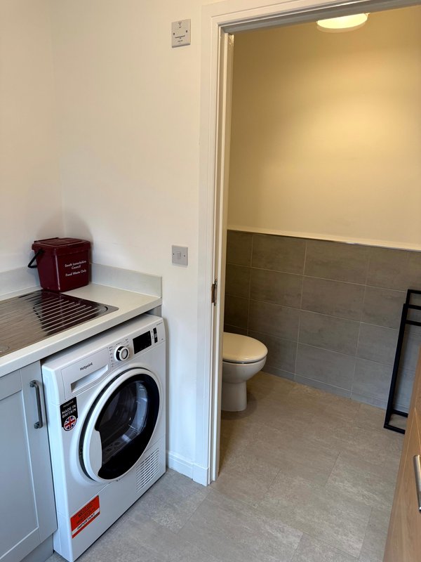 Utility room with washing machine and adjacent bathroom with toilet and tiled walls
