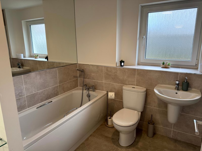 Clean bathroom with bathtub, toilet, sink, tiled walls and window