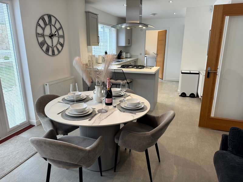 Open-plan dining and kitchen area with round white table, grey chairs, and modern appliances