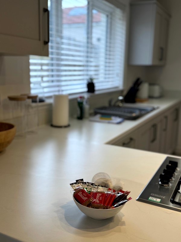 Kitchen with white countertop, window with blinds, appliances and bowl of decorative items