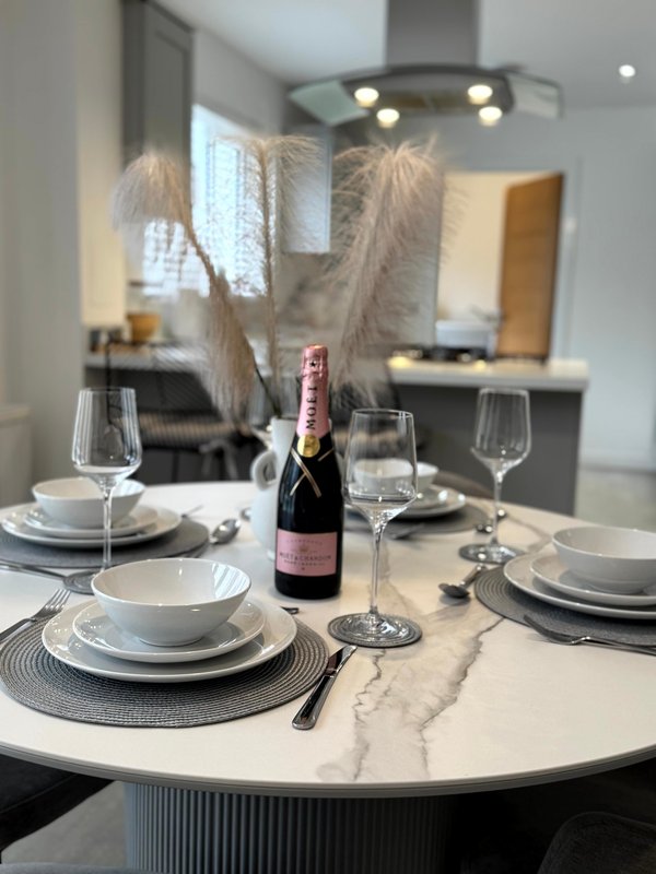 Dining table set for four with wine bottle, glasses, plates and pampas grass centerpiece