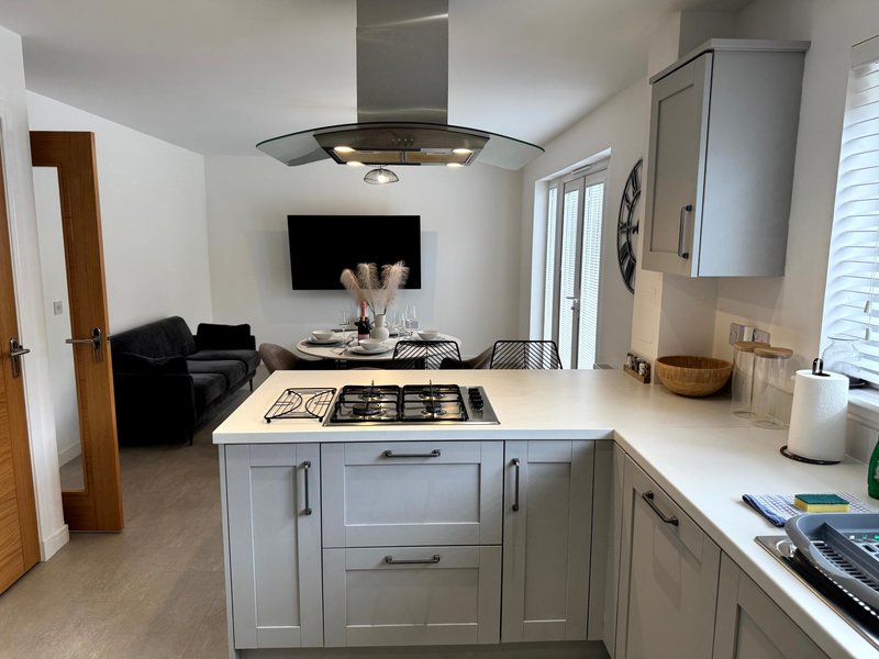 Modern open-plan kitchen and living room with white island, cooktop, and grey cabinetry