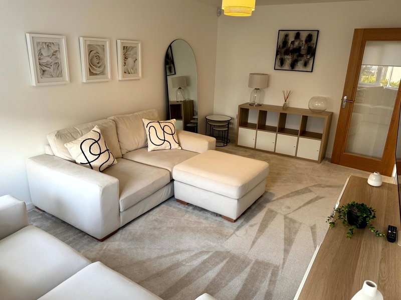 Modern living room with cream sectional sofa, geometric patterned rug, wall art and storage shelving
