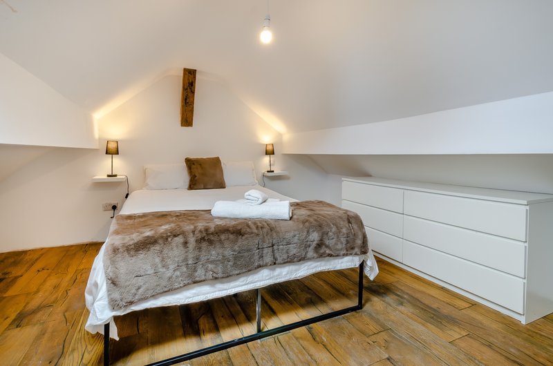 Attic bedroom with double bed, fur throw, wooden floor and white storage
